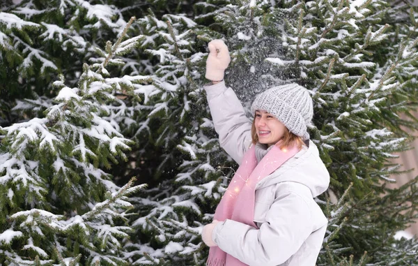 少女は雪を楽しんでいます ガーランドと緑のクリスマスツリーのそばに立って 雪に覆われた森の中の若い女性の冬の写真 — ストック写真