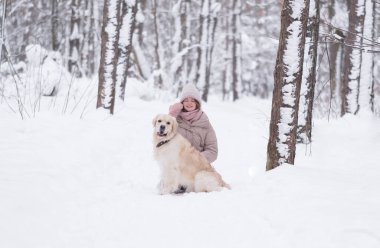 Genç kızıl saçlı bir kadın kış ormanında köpeğiyle oynuyor. Güzel bir kız, karla kaplı güzel bir parkta Golden Retriever 'la yürüyor. Bir evcil hayvanla arkadaşlık kavramı.