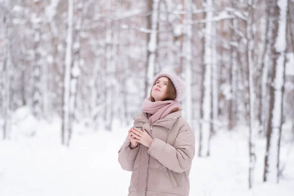 雪に覆われた冬の森の中で魔法瓶からお茶を飲む若い赤毛の女性 — ストック写真