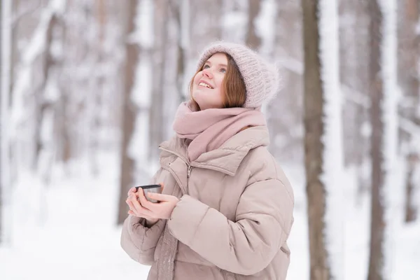 雪に覆われた冬の森の中で魔法瓶からお茶を飲む若い赤毛の女性 — ストック写真