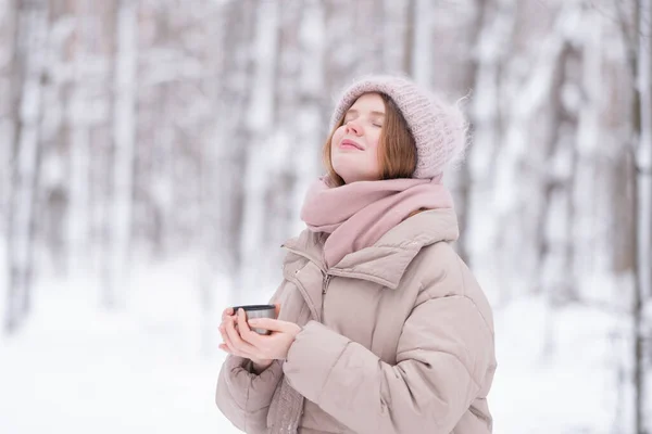 雪に覆われた冬の森の中で魔法瓶からお茶を飲む若い赤毛の女性 — ストック写真