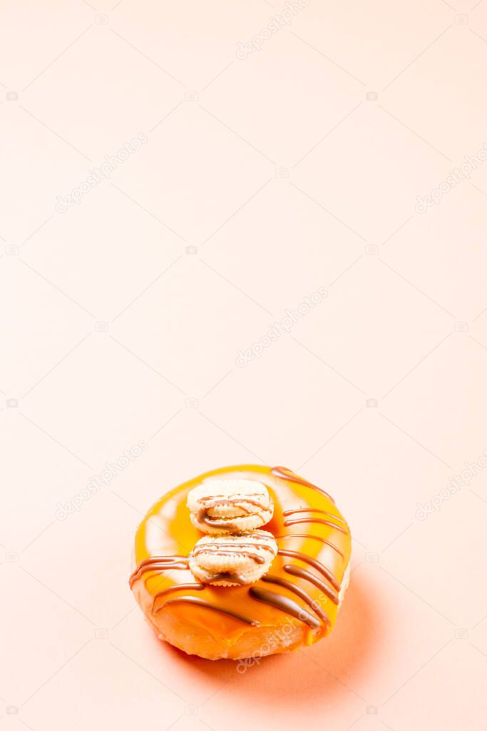 Photograph of a cream donuts decorated with two cookies and drawn with chocolate.The photo is taken vertically on a cream-colored background.The photo has copy space.
