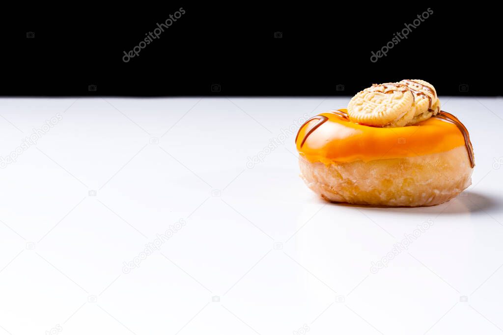 Close-up of a cream donuts painted with chocolate and cookies on a white table and a black background.The photograph is shot in horizontal format and has copy space.