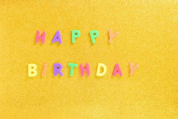 Photograph of some magnet letters with the English text of Happy Birthday on a golden background.The photograph is taken in horizontal format and from an overhead point of view. — Stock Photo, Image