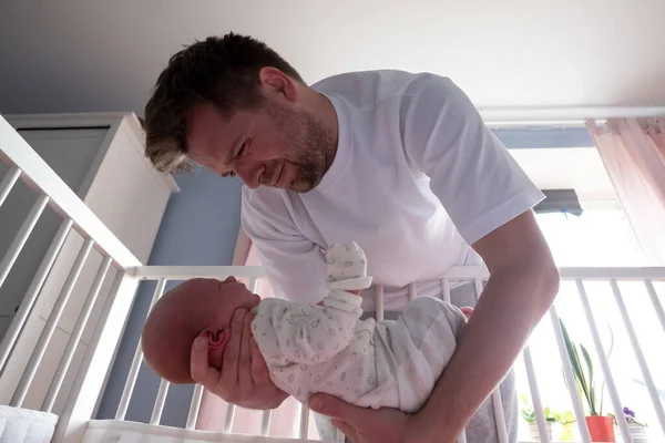 Jovem pai tentando acalmar seu bebê recém-nascido segurando-a em suas mãos. — Fotografia de Stock