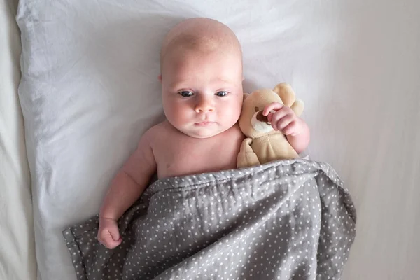 Niño sonriendo descansando en la cama con su osito de peluche. — Foto de Stock