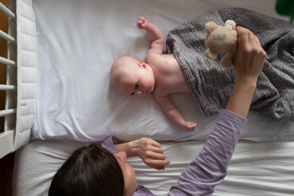 Niño y su madre descansando en la cama jugando con su osito de peluche. —  Fotos de Stock