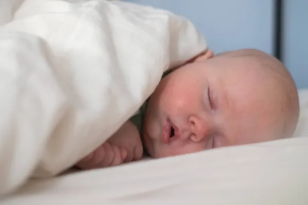 Baby sleeping on white sheets in bed with a blanket. — Stock Photo, Image