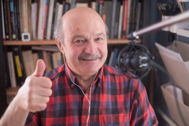 Emekli kıdemli blogcu kamera kaydına bakıyor, gülümseyen yaşlı büyükbaba baş parmağını gösteriyor.