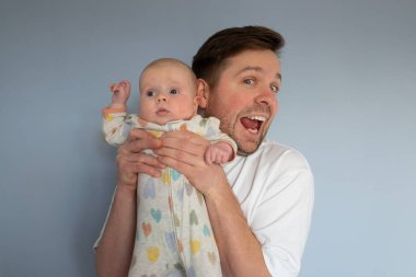 Elinde 3 aylık bir bebek tutan genç adam, mavi arka planda izole edilmiş.