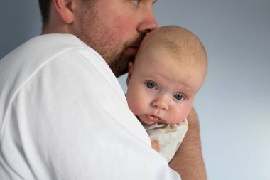 Elinde 3 aylık bir bebek tutan genç adam, mavi arka planda izole edilmiş.