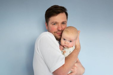 Elinde 3 aylık bir bebek tutan genç adam, mavi arka planda izole edilmiş.