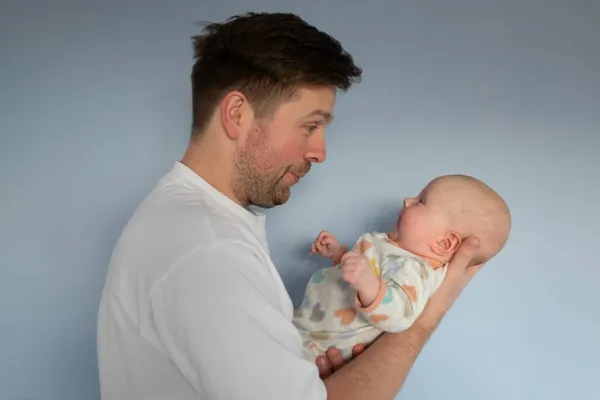 Young man holding a 3months old baby, isolated on blue background — Stock Photo, Image