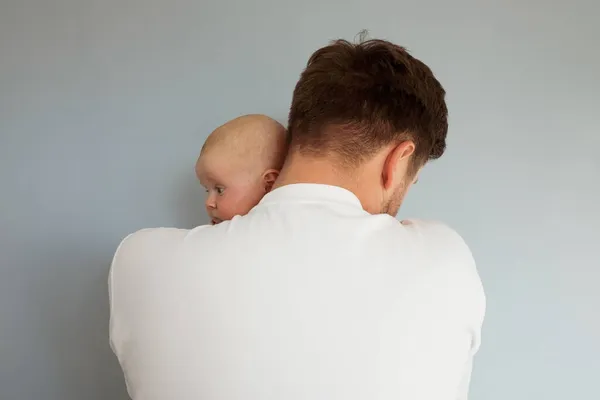 Triste jeune homme tenant un bébé de 2 mois, isolé sur fond bleu — Photo