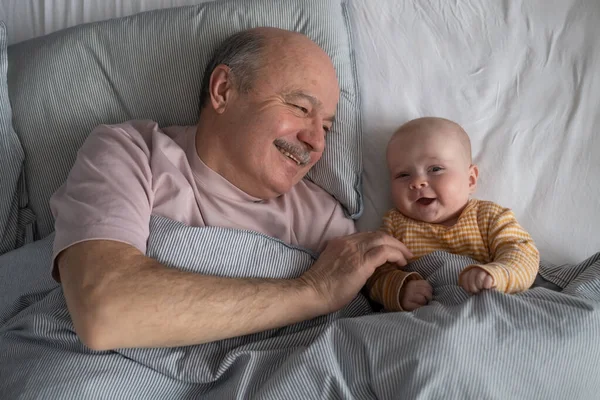 Cheerful senior grandfather resting with his grandson on bed at the morning having a nap — Stock Photo, Image