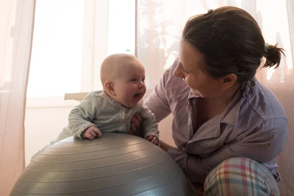 Moeder en haar baby meisje hebben plezier met gymnastiek bal. — Stockfoto