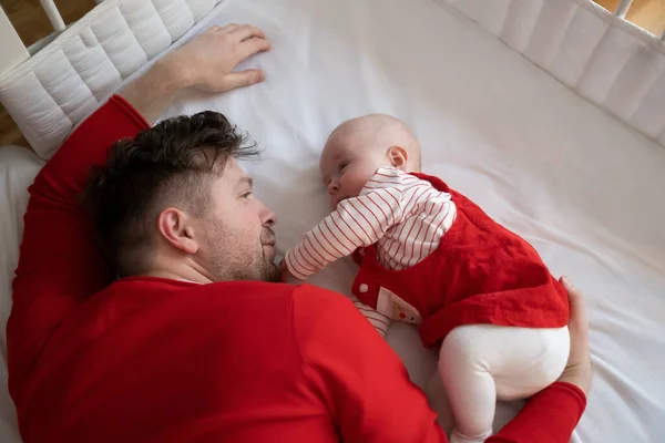Ayah dengan bayi perempuannya dalam gaun Natal beristirahat di tempat tidur. — Stok Foto