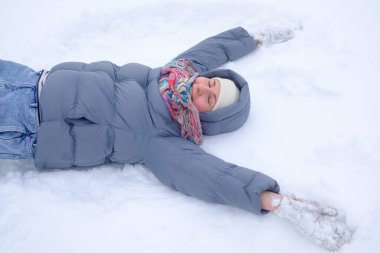 Genç bir kadın karda uzanıp kollarını aşağı yukarı hareket ettiriyor ve bir melek figürü yaratıyor.