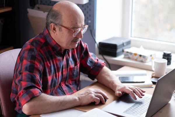 Старший мужчина в очках с ноутбуком дома поиск в Интернете — стоковое фото