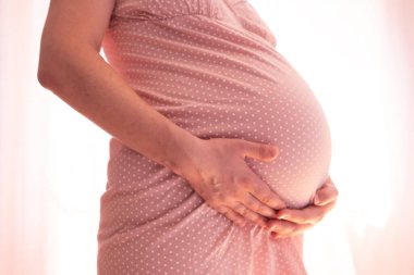 Hamile kadın pencerenin yanında karnına dokunuyor..