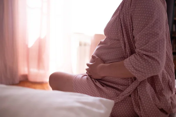 Woman suffering from pains at home, sitting at bed, touching her tummy and back, expecting lady having childbirth labo — Stock Photo, Image