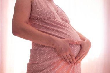 Hamile kadın pencerenin yanında karnına dokunuyor..