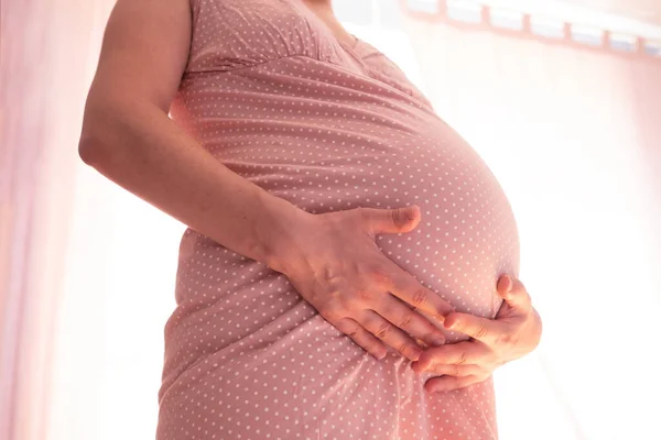 Mulher grávida tocando barriga de pé perto da janela. — Fotografia de Stock