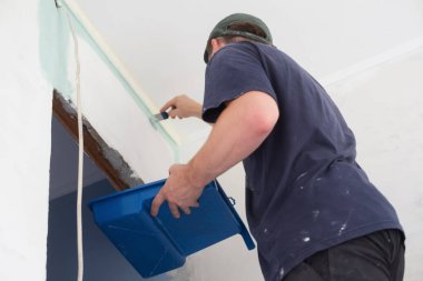 Boyalı silindirle duvar boyayan bir adam..