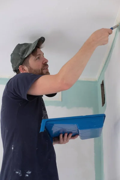 Hombre pintando una pared de la casa con un rodillo de pintura. — Foto de Stock