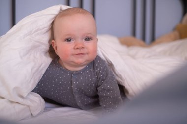 Sevimli, mutlu, beyaz, altı aylık bebek bezi takmış, yalan söylüyor ve oynuyor.