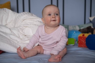 Sevimli, mutlu, beyaz, altı aylık bebek bezi takmış, yalan söylüyor ve oynuyor.