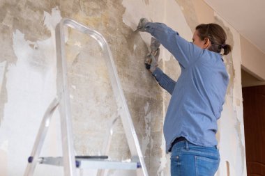 Kafkasyalı hamile bir kadın duvarlardan eski duvar kağıtlarını söküyor ve tadilata hazırlanıyor..