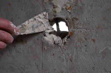 İşçi duvardaki deliği tamir ediyor, mala sıva yayıyor.