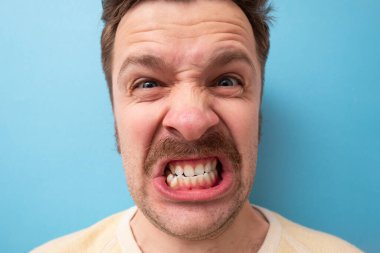 Bıyıklı, kızgın ve öfkeli bir beyaz adam. Stüdyo resmi mavi duvarda.