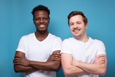 İki genç adam kollarını kavuşturup kameraya gülümsüyor..