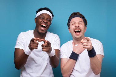 İki neşeli genç adam mavi arka planda dikilip gülüyorlar.