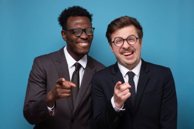 Takım elbiseli iki genç Afrikalı ve beyaz adam kollarını kavuşturup kameraya gülümsüyor..