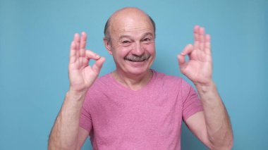 Orta yaşlı adam olumlu gülümsüyor, tamam işareti onaylıyor. Olumlu yüz insani duygu.