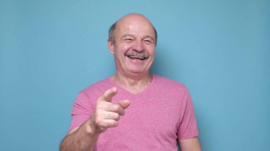 Üst düzey İspanyol adam sana gülüyor, kamerayı işaret ediyor. Stüdyo resmi mavi duvarda