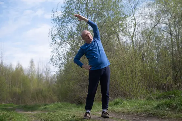 Kolluk takan kıdemli koşucu esneme hareketleri yapıyor. Bahar doğası. Yaşlılıkta sağlıklı bir yaşam tarzı.