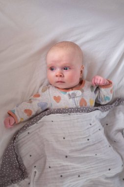 Küçük beyaz bir çocuk yatağa uzanmış kameraya bakıyor.