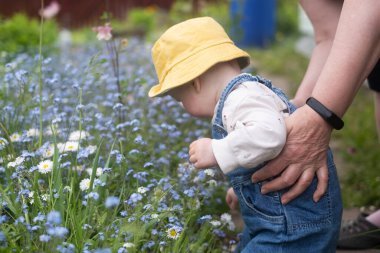 Küçük çocuk eğleniyor ve doğayı keşfediyor. Çiçek çayırında neşeli bir kız bebek. Mutlu çocukluk ve çocuk bakımı