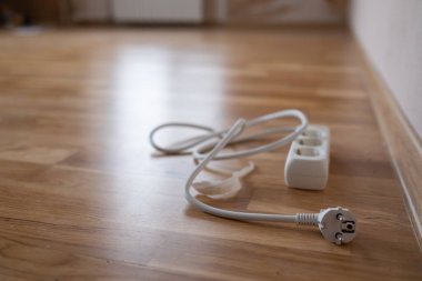 Beyaz çoklu prizli elektrik kablosu ve uzun kabloyla evdeki ahşap zemindeki güç kaynağı kablosunu uzatıyor.