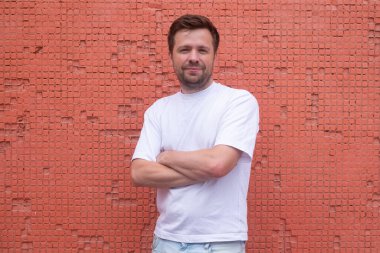 Kırmızı arka planda çapraz pozlar veren kendine güvenen genç erkek model.