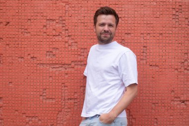 Kırmızı arka planda çapraz pozlar veren kendine güvenen genç erkek model.