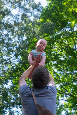 Küçük kızını kucaklayan genç bir babanın açık hava portresi.