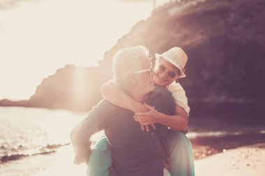 Kıdemli çift sahilde eğleniyor, kıdemli adam karısını sırtında taşıyor ve yaz tatilinde eğleniyor..