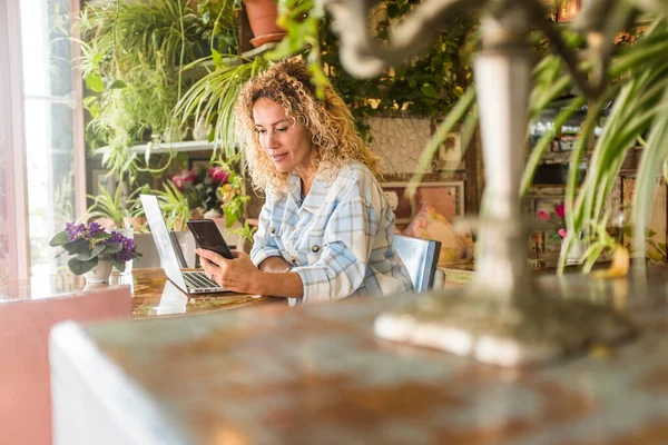 Happy young woman working on laptop and text messaging on mobile phone.