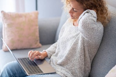 Dizüstü bilgisayarla kanepede otururken boynuna masaj yapan güzel bir genç kadın.. 