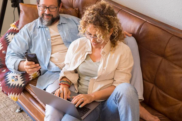 Glad Kvinde Bruger Laptop Sidder Sofaen Derhjemme Med Sin Mand - Stock-foto